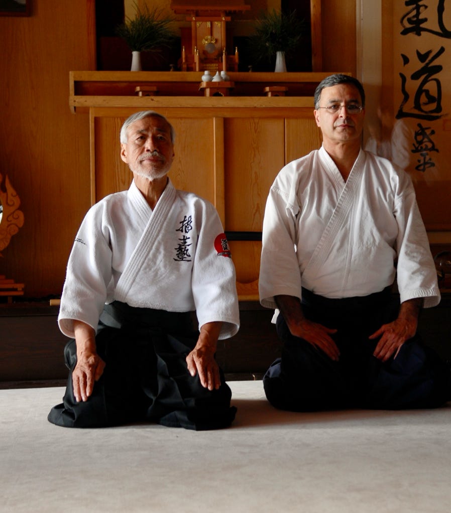 Child practicing a high kick in martial arts dojo wearing a blue belt.