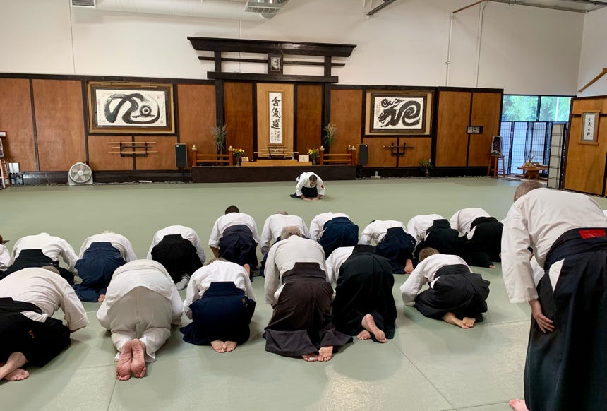 Two adults practicing martial arts in a dimly lit studio, holding traditional weapons.