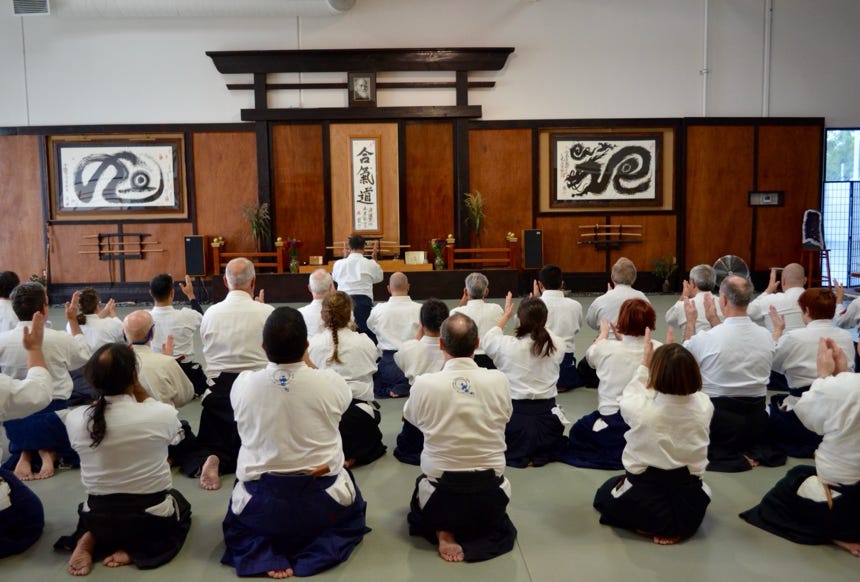 Two adults practicing martial arts in a dimly lit studio, holding traditional weapons.